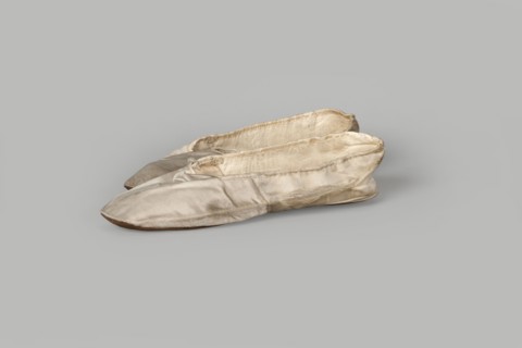 Flat women's slippers of white satin with top edge finished with ribbon. Flat-cut toes, symmetrical