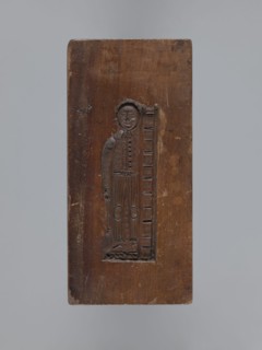 Double-sided gingerbread form. Side A: female figure with a scarf on her head, standing, leaning on