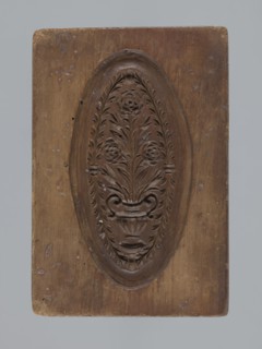 Double-sided gingerbread mould. Obverse: oval frame containing a decorative vase with flowers