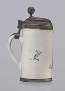 Cylindrical tankard in a pewter frame. White faience painted in colors. From the front, a barefoot