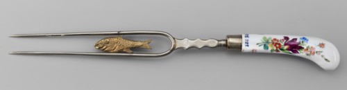 Two-pronged fork with a gilded plastic fish between the tines and a plastic palmette at the base;
