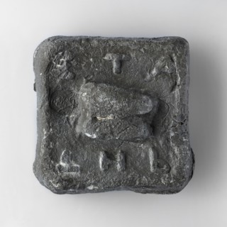Square weight with diagonally cut side edges. The upper surface is decorated with a plastic