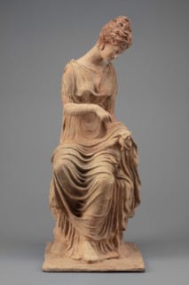 Figurine of a woman sitting on a rock with a flower in her hand. Woman sitting on a rock with a