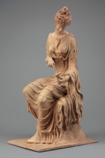 Figurine of a woman sitting on a rock with a flower in her hand. Woman sitting on a rock with a