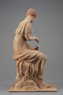 Figurine of a woman sitting on a rock with a flower in her hand. Woman sitting on a rock with a