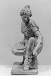 Terracotta figurine of a girl throwing dice. Figurine of a crouching girl throwing dice: the weight