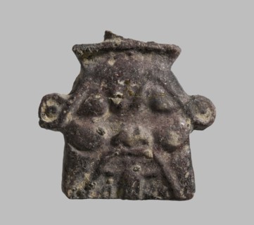 Plaque with a schematic relief representation of the head of Bes. The crown has been knocked off,