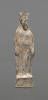 Female terracotta figurine of a standing woman, depicted frontally. Set on a small hollow,