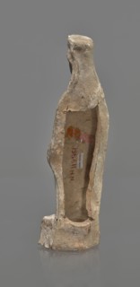 Female terracotta figurine of a standing woman, depicted frontally. Set on a small, hollow,