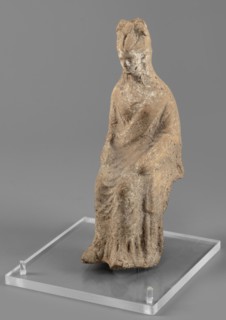 Female figurine in a seated position, slightly leaning forward. The back of the figurine is not