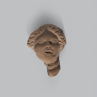 Head of a terracotta female figurine with part of the neck and a fragment of a robe preserved.
