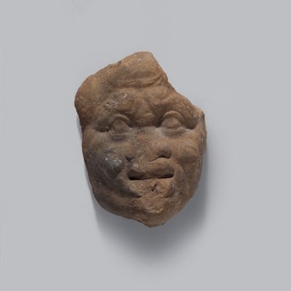 Head of a man. Fragment of a terracotta figurine of a man in a caricatured style. The face is wide