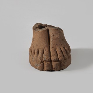 Fragment of a terracotta figurine showing two feet placed side by side on a flat, rounded base.,