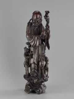 Deity of Longevity Shouxing/Shoulao holds a long traveling staff and a peach of immortality; his