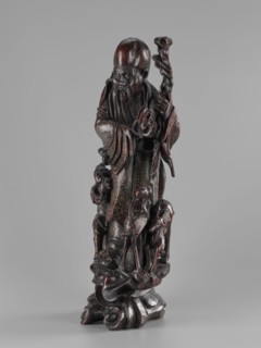 Deity of Longevity Shouxing, Shoulao holds a long traveling staff and a peach of immortality; his