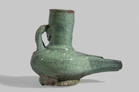 Jug-shaped oil lamp with a handle at the neck and a long burner, covered with a turquoise glaze on