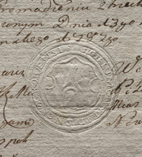Round seal impression of the town of Nawogród. In a Baroque cartouche, a wall with a gate and three