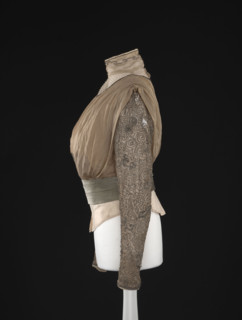 Blouse. Made of beige-gold muslin, short, bloused, fitted at the waist with a belt draped in three