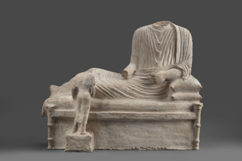 Depiction of a deceased person on a keline and a servant. The sculpture depicts a man banqueting in