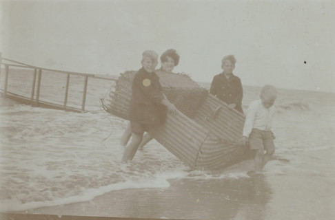 Koosje, Daan and Ben Ochse and another boy carrying a wicker beach chair out of the sea,