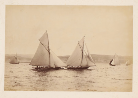 Various sailing ships, including Woodcock and Yvonne, at sea with a hilly landscape in the