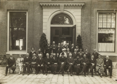 Group portrait of men and women in front of the entrance of a building, photograph, stamp: