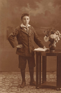 Studio portrait of an unknown boy next to a table, photograph, postcard, photographer: Machiel