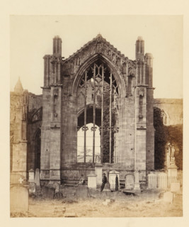 View of a window of the ruins of Melrose Abbey with two men in front of it, photograph, page,