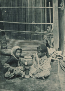 Tunisia, Carpet Manufacturer, Two children playing in front of a woman behind a loom in the