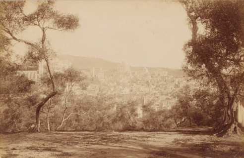 View from a park ? of houses of a place partially situated on a hill and trees on either side,