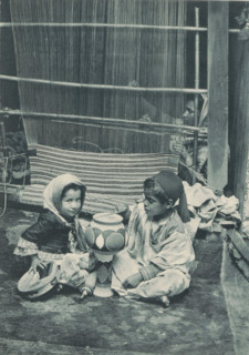 Two unknown Tunisian children in front of an unknown woman weaving a carpet, Tunisia - fabricante