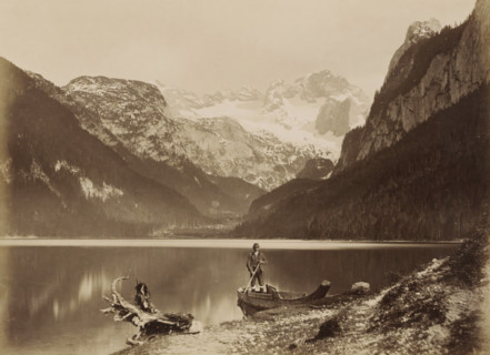 View of a lake and surrounding mountains with a man standing in a boat in the foreground,