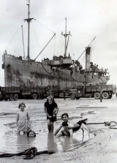 Fillettes jouant sur une plage d'Arromanches, devant un bateau allié