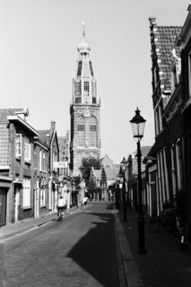 La tour de la Zuiderkerk au bout d'une rue bordée de maisons, avec un lampadaire au premier plan.