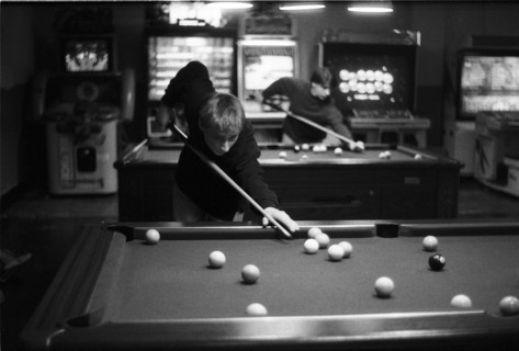 Player leaning over a pool table in an amusement arcade, with arcade machines at the back.