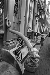 Rampe ornementale à volutes en fer forgé, dont l'extrémité est sculptée, devant une façade.