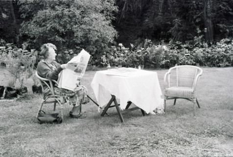 Person reading in a garden, next to a table covered with a white tablecloth.
2000