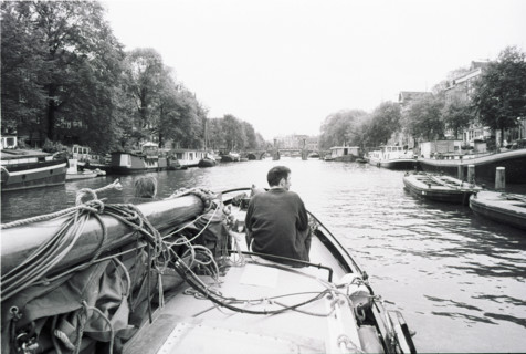 Canal d'Amsterdam vu depuis l'avant d'un bateau, une personne assise à la proue. Amsterdam,