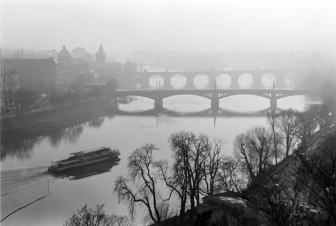 Brume sur la Vltava : un bateau sur l'eau, un pont en arrière-plan et des arbres sur la rive.