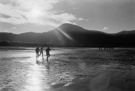 Runners on a beach against the light, with Croagh Patrick mountain in the background. County Mayo,