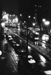 Rue éclairée de nuit, avec des voitures en circulation et des reflets de lumière sur la chaussée.