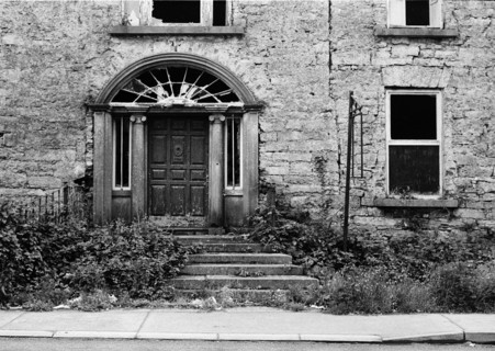 The façade of an old stone house with a door surmounted by a fan-shaped transom window. Ireland