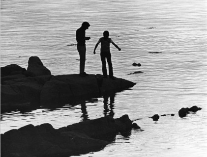 Two silhouettes on rocks at the water's edge, against the light. Dún Laoghaire, Dublin, Ireland