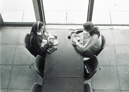 Deux jeunes femmes déjeunant face à face à une table de la cantine, vues en plongée. University