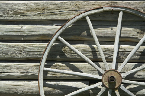 Wagon wheel against wooden wall.