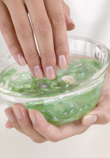 Female fingers in a dish of aloe gel.
