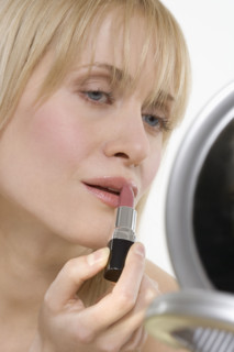 Woman with mirror applying lipstick.