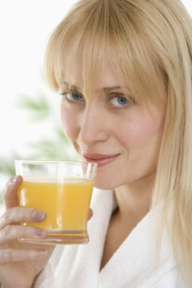 Woman in bathrobe drinking orange juice.