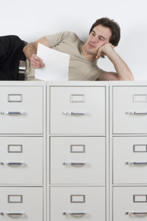 Man reading lying atop file cabinets.