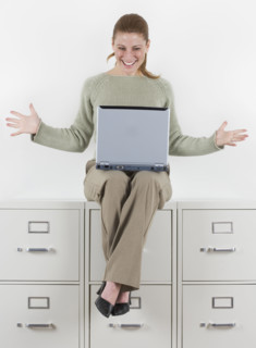 Woman with laptop atop file cabinets.